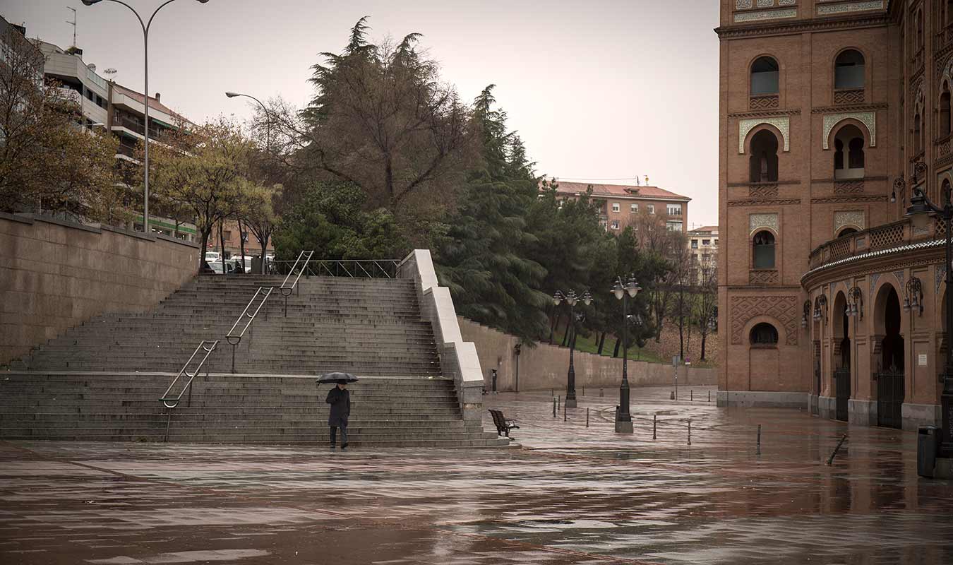 Foto del exterior de la plaza de las ventas, llueve y un señor baja las escaleras con un paraguas
